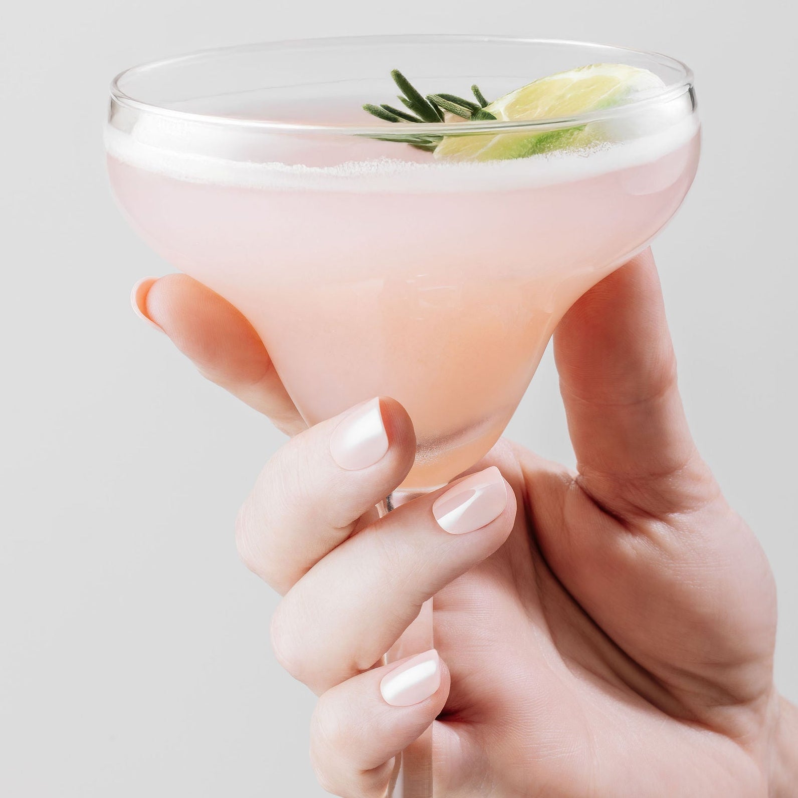 Hand holding a cocktail glass with a light pink nails